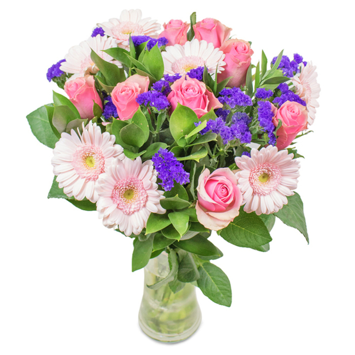 A radiant, thoughtfully designed bouquet in a sleek clear glass vase stands out against a crisp white background-the sort of arrangement beloved across West Ham. Its centre is a cluster of seven to nine soft and medium pink roses, some petals just now beginning their gentle spiral outward. These are complemented beautifully by five to seven pale pink Gerbera daisies, noted for their large, round blooms and almost white, softly glowing centres. Sprays of lively purple statice weave through the arrangement, lending a dramatic contrast that draws out the vibrancy of each shade and calls to mind the creative flair of local flower markets. Below, rich green foliage cradles the bouquet, its abundant texture evoking the tree-lined avenues of West Ham and a pervasive freshness. The stems, visible below the water line in the vase, give a nod to the care and immediacy of same-day local delivery. Perfect for commemorating birthdays, anniversaries, or as a cheer-bringing accent in the home or office, this bouquet celebrates West Ham's warmth and sense of heartfelt connection, expertly crafted by local florists.